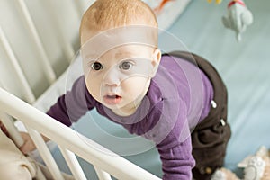 Top view of adorable baby trying to stand up in his cot