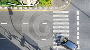 Top view aerial photo of a driving car on asphalt track and pedestrian crosswalk in traffic road with light and shadow silhouette