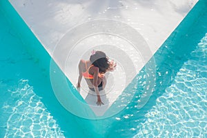 Top view aerial photo of model in bright swimwear relaxing in hotel pool during her summer weekend