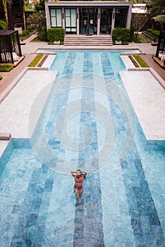 Top view aerial photo of a seductive model in white swimwear is enjoying relax in hotel pool during her summer