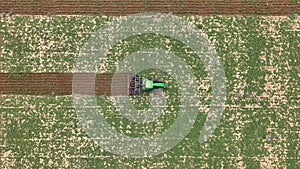 Top view of an agricultural tractor crossing a field right down the center, from left to right, tilling a field creating furrows