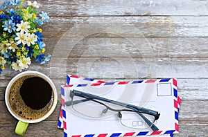 Top view with air mail envelope,cup of coffee,glasses and flower on wood table background