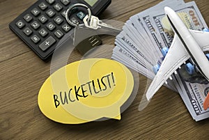 Top view of airplane model , money, house key, calculator and yellow speech burble written with Bucketlist on wooden background photo