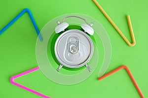 Top view of alarm-clock soda can and multicolored drinking straws abstract on green