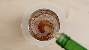 Top view of alcoholic beverage being poured in a glass with ice cubes on wooden table, whiskey drink