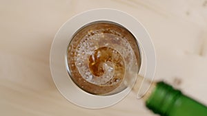 Top view alcoholic drink being poured in glass with ice cubes on wooden table, rum or whiskey drink