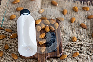 Top view of almond milk with sesame in a plastic bottle with almonds nut and sesame seeds on rustic fabric wooden tray and table.