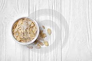 Top view of almond slices in white bowl on wooden background