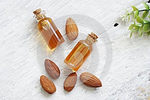 Top view of almonds oil in clear glass and pile of roasted almonds on white wooden .