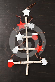 Top view of alternative Christmas tree made of birch branches and different wooden decoration on dark brown background