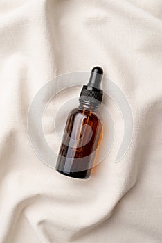 top view of amber glass essential oil droppper bottle with pipette on fabric wavy background