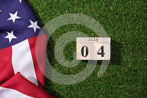 top view of american flag and wooden calendar with 4th july date on green lawn, americas independence