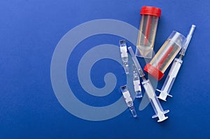 Top view of ampules, syringes and plastic urine containers with samples on the dark blue background.Empty space for text.Concept o