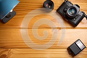 Top view of analog camera, flash and lens on wooden table, professional photography equipment. Photography background with copy sp