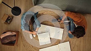 Top view of apartment living room. Man and woman assembles furniture, woman sits upset man looking at furniture details.