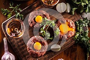 Top view of appetizing beef steak tartare with delicious egg yolk and alcohol. Served on a wooden desk with onion and herbs