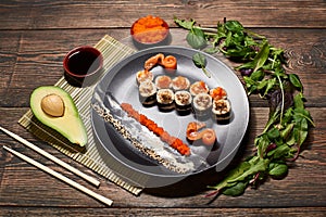 Top view of appetizing Japanese sushi rolls in big black plate, serving with fish slices, sauces, caviar, avocado, salad