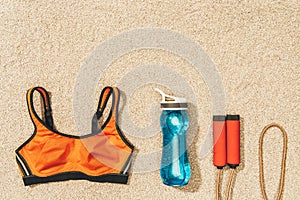 top view of arranged sportswear, skipping rope and water bottle on sand