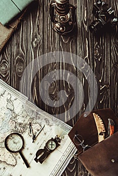 top view of arrangement with map, magnifying glass, bag, compass and retro photo camera on dark