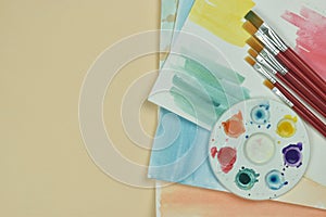 Top view of art palette, watercolor and a brush on orange background and copy space. Art and craft tools