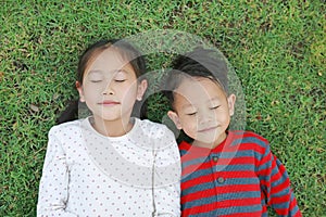 Top view Asian little child boy and girl lying on green grass outdoors in summer park. Portrait of sister and brother closed eyes