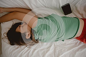 Top view of asian Thai woman lying on white couch, tired resting alone with mobile phone on sofa in room apartment.