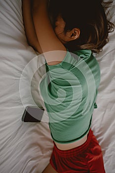 Top view of asian Thai woman lying on white couch, tired resting alone with mobile phone on sofa in room apartment.