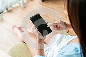 Top view of Asian woman relaxing on sofa at home in the morning while using mobile phone with blank screen for text. Technology