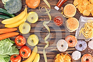 top view of assorted junk food, fresh fruits with vegetables and measuring tape on wooden