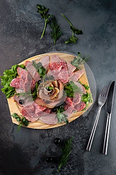 Top view assorted sliced delicious meat mix as salami, bacon and ham with parsley and olives on a wooden cutting board on grey