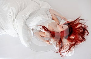 Top view of attractive, young, red-haired woman relaxing in bed, enjoying fresh soft sheets in bedroom, copy space