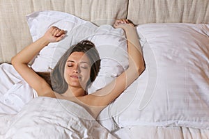 Top view of attractive young woman sleeping well in bed hugging soft white pillow. Teenage girl resting, good night sleep concept.