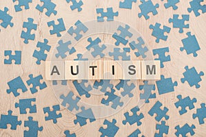 Top view of autism lettering made of wooden blocks among blue puzzle pieces on wooden table.