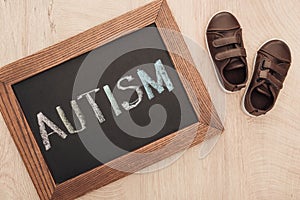 Top view of autism lettering written on chalkboard near children brown sneakers on wooden surface.