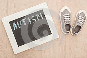 Top view of autism lettering written on chalkboard near children grey sneakers on wooden surface.