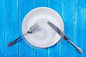 Top view background with empty white ceramic plate, antique silver cutlery on vintage weathered blue wooden boards