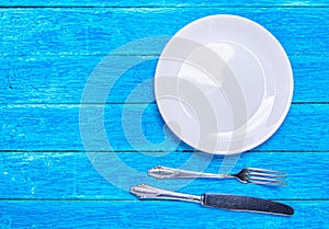 Top view background with empty white ceramic plate, antique silver cutlery on vintage weathered blue wooden boards