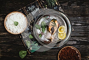 Top view of baked salmon steak with lemon on rustic metal tray with rice side dish