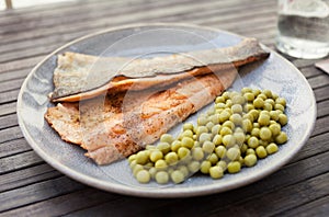 Top view of baked trout fillet served on plate with peas closeup
