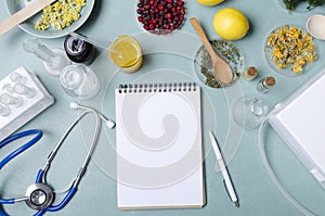 Top view of balnk doctor`s notebook, stethoscope, herbs, tubes and other medical glassware on the blue table.Concept of traditiona