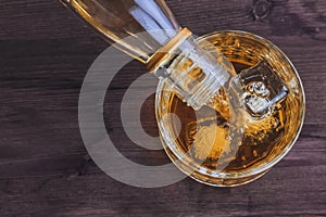 Top of view of barman pouring whiskey in the glass with ice cubes on wood table background, focus on ice cubes