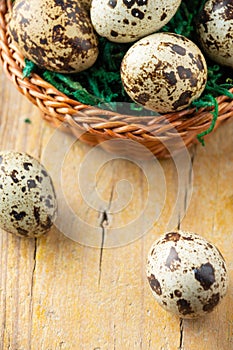 Top view of basket with quail eggs on wooden table with two eggs, selective focus, vertical