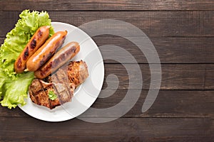 Top view BBQ Grilled meat, sausages and vegetables on dish on wooden background. Copy space for your text
