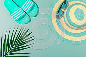 Top view on beach accessories on turquoise blue background - sunglasses, blue flip-flops, striped hat and palm leaf