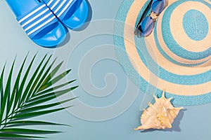 Top view on beach accessories on turquoise blue background - sunglasses, blue striped hat and palm leaf. Concept of