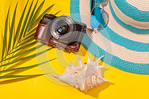 Top view on beach accessories on yellow background - sunglasses, striped blue hat, camera, sea shell and palm leaf