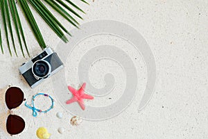 Top view of beach sand with coconut leaves, camera, bracelet made of seashells, sunglasses, shells and starfish.