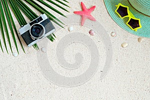 Top view of beach sand with coconut leaves, camera, shells, starfish, sunglasses, shells and straw hat.