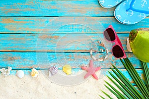 top view of beach sand with slipper, coconut, sunglasses, coconut leaves, starfish, shells, coral and bracelet made of seashells