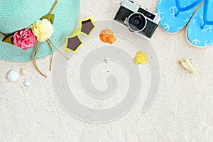 Top view of beach sand with straw hat, sunglasses, shells, camera, slippers and coral.